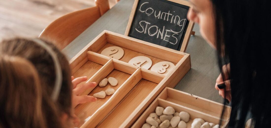 A child placing smooth stones into numbered wooden trays during a counting activity at Treehouse Nursery