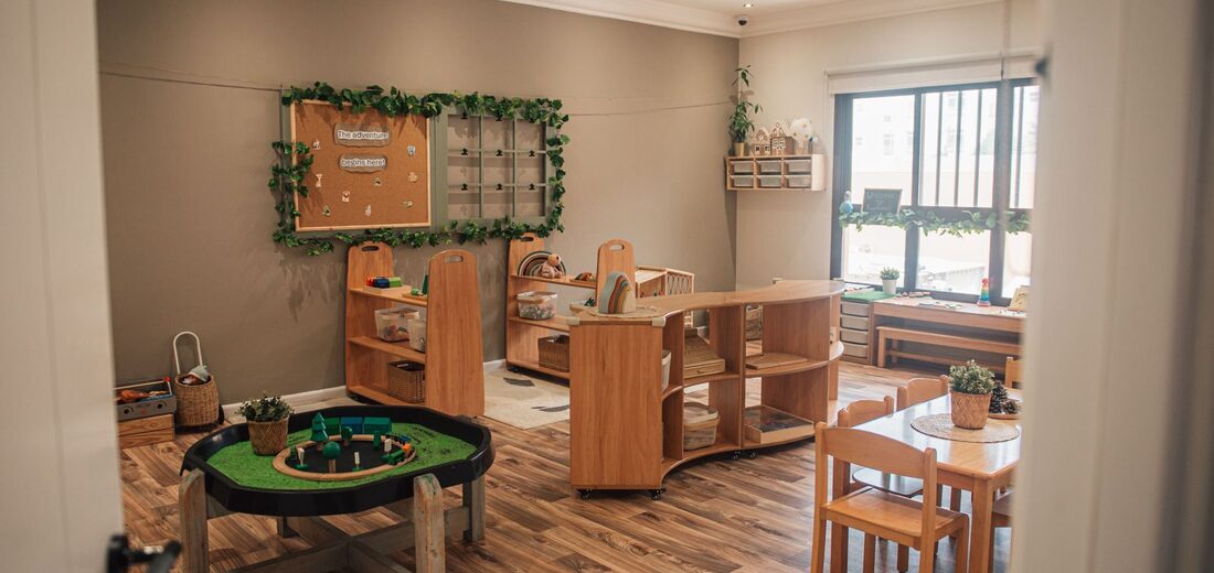 A Treehouse Nursery classroom with wooden shelving, a small-world play tray and child-sized tables by the window