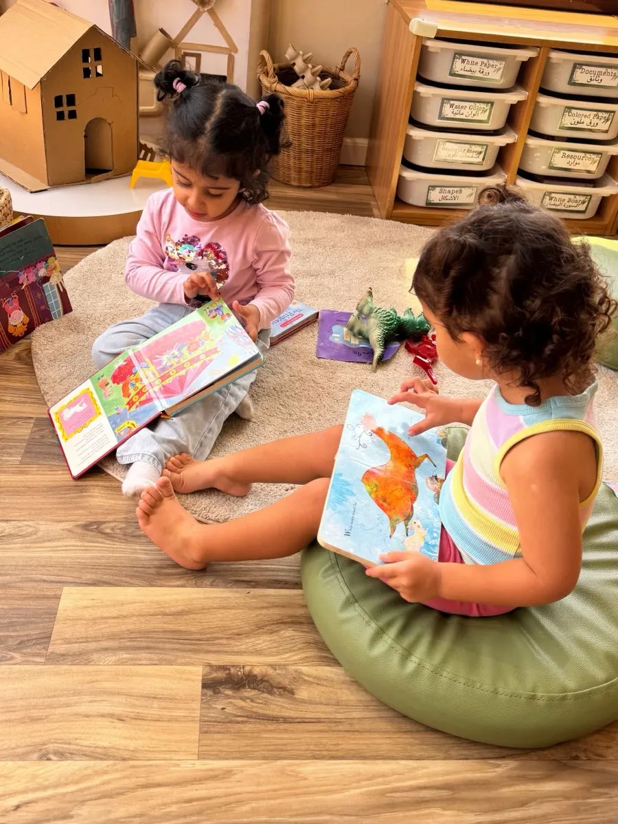 Two children sitting on floor cushions looking through picture books in a Treehouse Nursery classroom