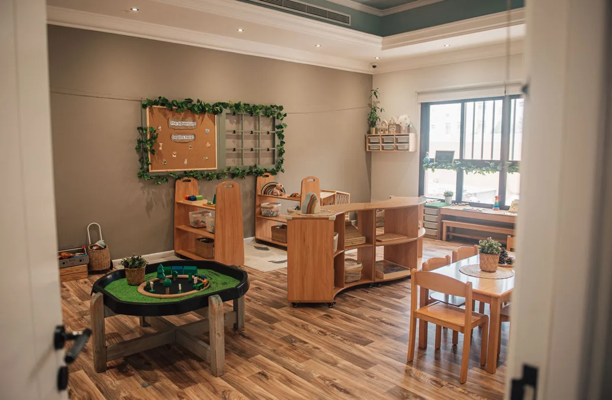 Empty nursery classroom with tuff tray, wooden shelving, low tables and a display board