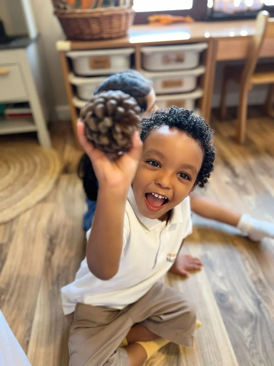 A smiling child holding up a pine cone found on a nature hunt