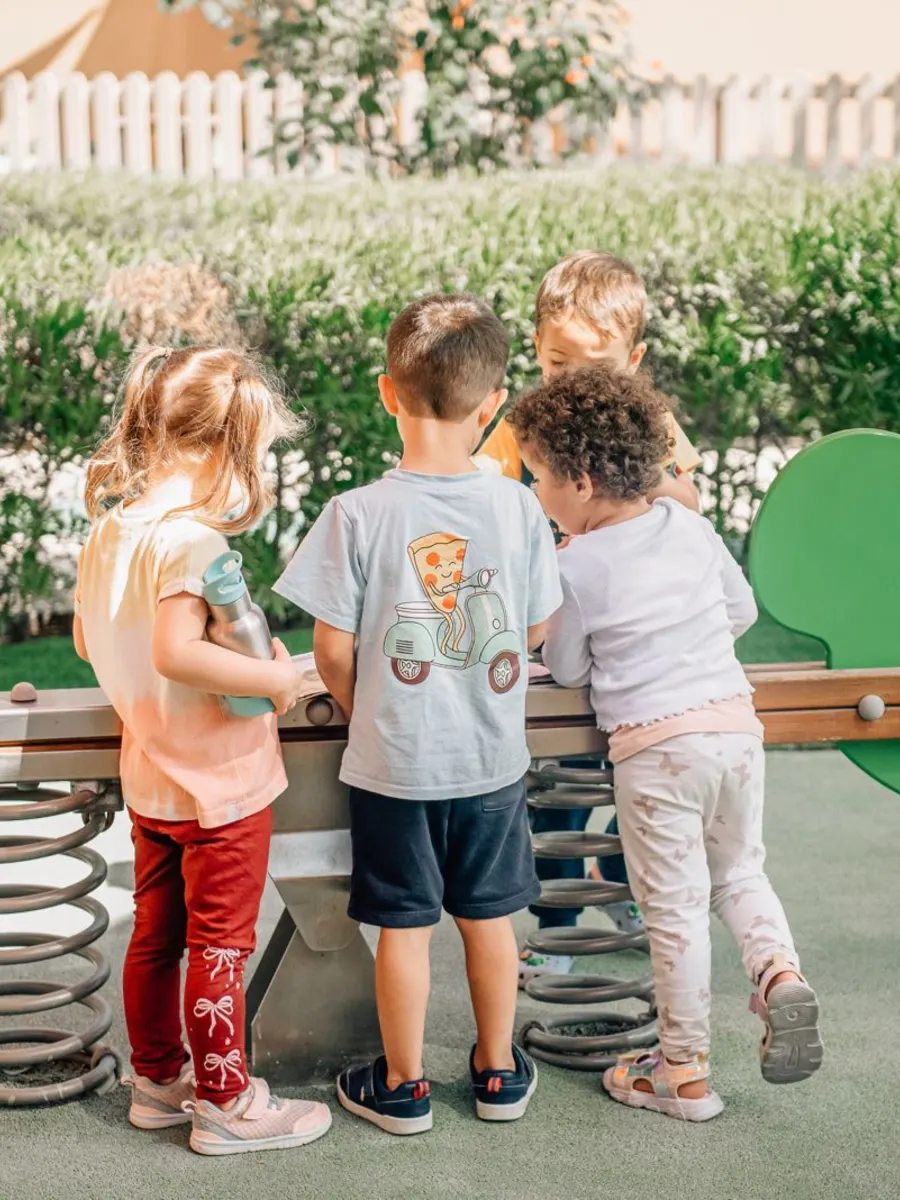 Three children playing together on a spring rider in the shaded outdoor play area