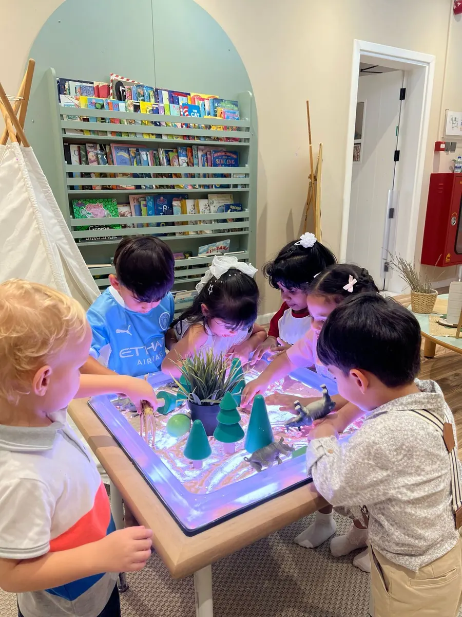 Children gathered around a glowing light table with small trees and figures