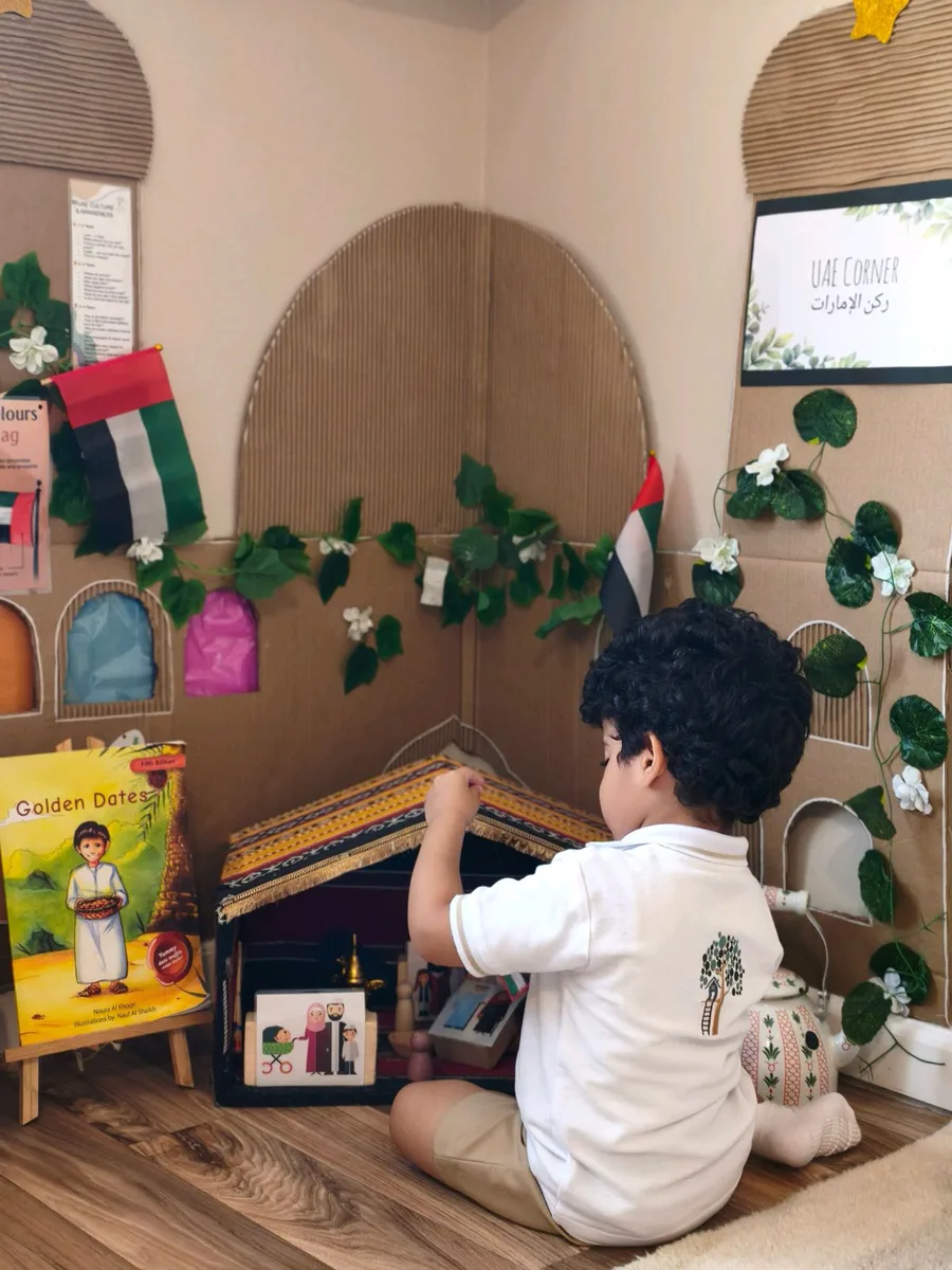 Child playing at a cardboard UAE corner with majlis, flags and Emirati story books